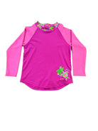 A pink long-sleeve rash guard swimsuit with a colorful floral pattern around the collar and a turtle graphic on the lower right, laid flat on a wooden table.